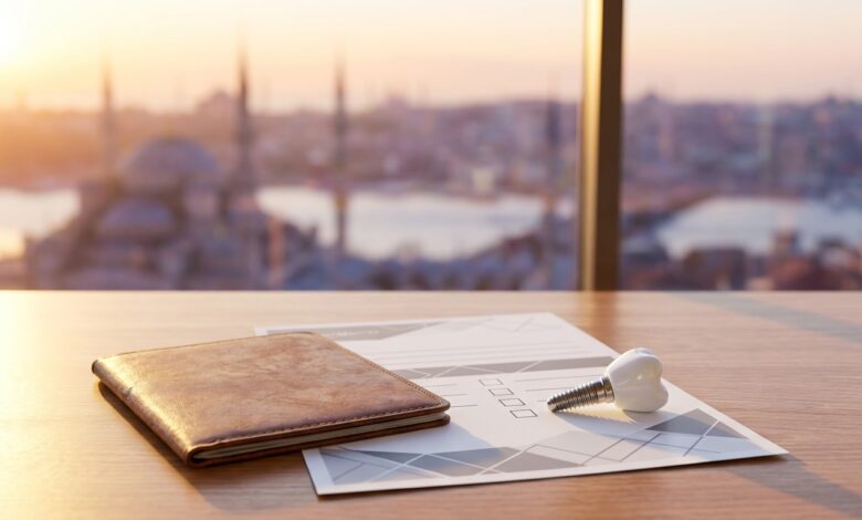 Conceptueel beeld over tandheelkundig toerisme en zorgverzekering, met een paspoort, een leeg formulier en een tandimplantaatmodel op een bureau, tegen een wazige achtergrond van de skyline van Istanbul.
