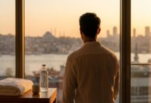 Een man kijkt vanuit een moderne, luxe kamer uit over de skyline van Istanbul bij zonsopgang, wat de combinatie van een medische reis en een vakantie in Turkije symboliseert.