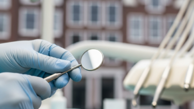 Een close-up van steriele handschoenen van een tandarts of kaakchirurg die een klein, reflecterend tandheelkundig instrument vasthouden. De setting is een zeer schone, modern verlichte tandartspraktijk. De achtergrond is extreem onscherp en toont de daken en gebouwen langs een typisch Nederlands grachtenpand, wat de locatie in Nederland aangeeft. De scène is helder en focust op professionele zorg.