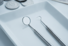 Een close-up van glanzende tandartsinstrumenten (spiegel, sonde, scaler) op een witte, reflecterende ondergrond, met op de achtergrond onscherpe financiële documenten en geld die de kosten en verzekeringsaspecten van tandzorg symboliseren.