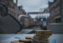 Afbeelding van euromunten en een bankbiljet op een oppervlak, met op de achtergrond een onscherpe tandartspraktijk en Nederlandse stadssilhouet, die de hoge en deels onvergoede kosten van tandheelkundige zorg symboliseert.